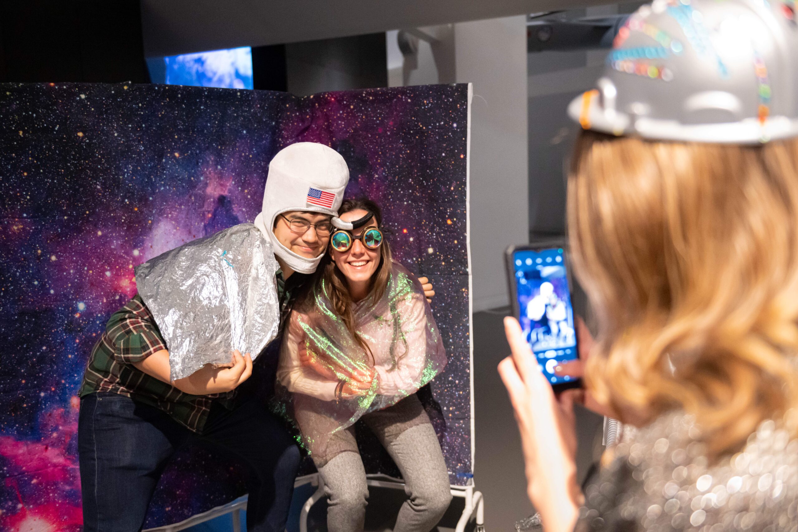 man and woman standing in front of fake space background with glasses and hat on getting their picture taken