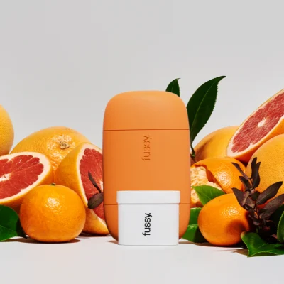 A orange cased Fussy deodorant with oranges in the background