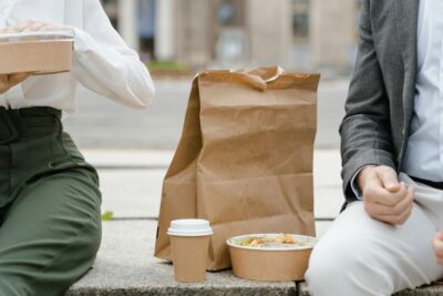 Two people having a brown bag lunch outside