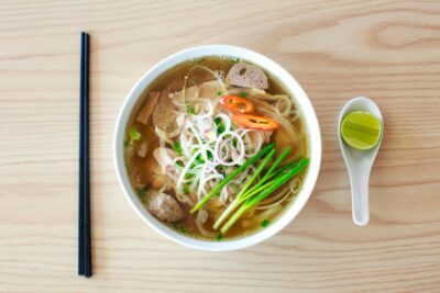 A bowl of both and meat with a spoon and chopsticks to the side