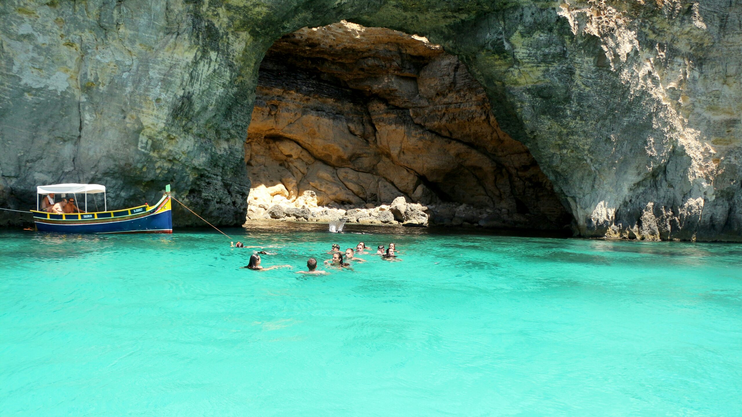 bright turquoise sea water in Malta with a boat socked and people swimming
