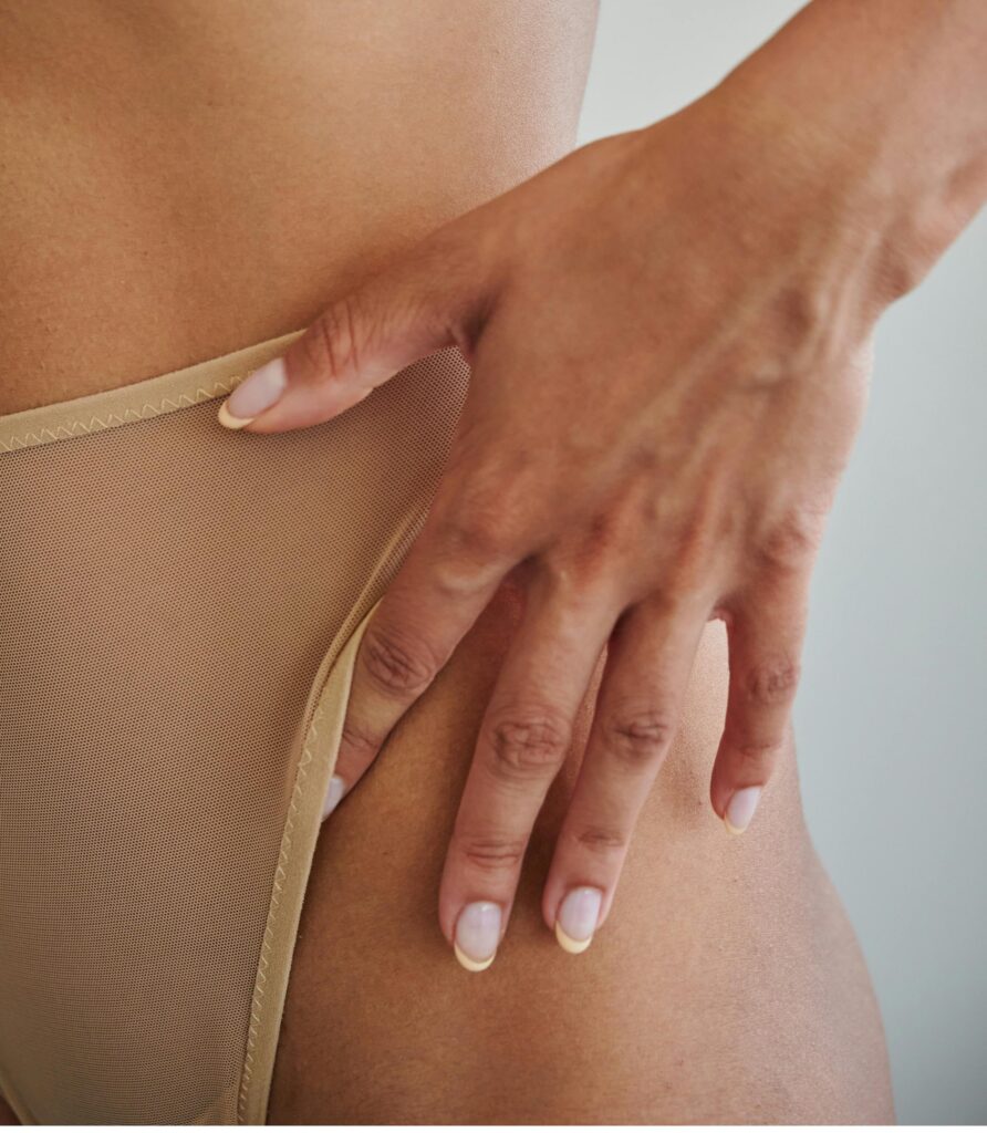 A woman rests her hand on her upper thigh 