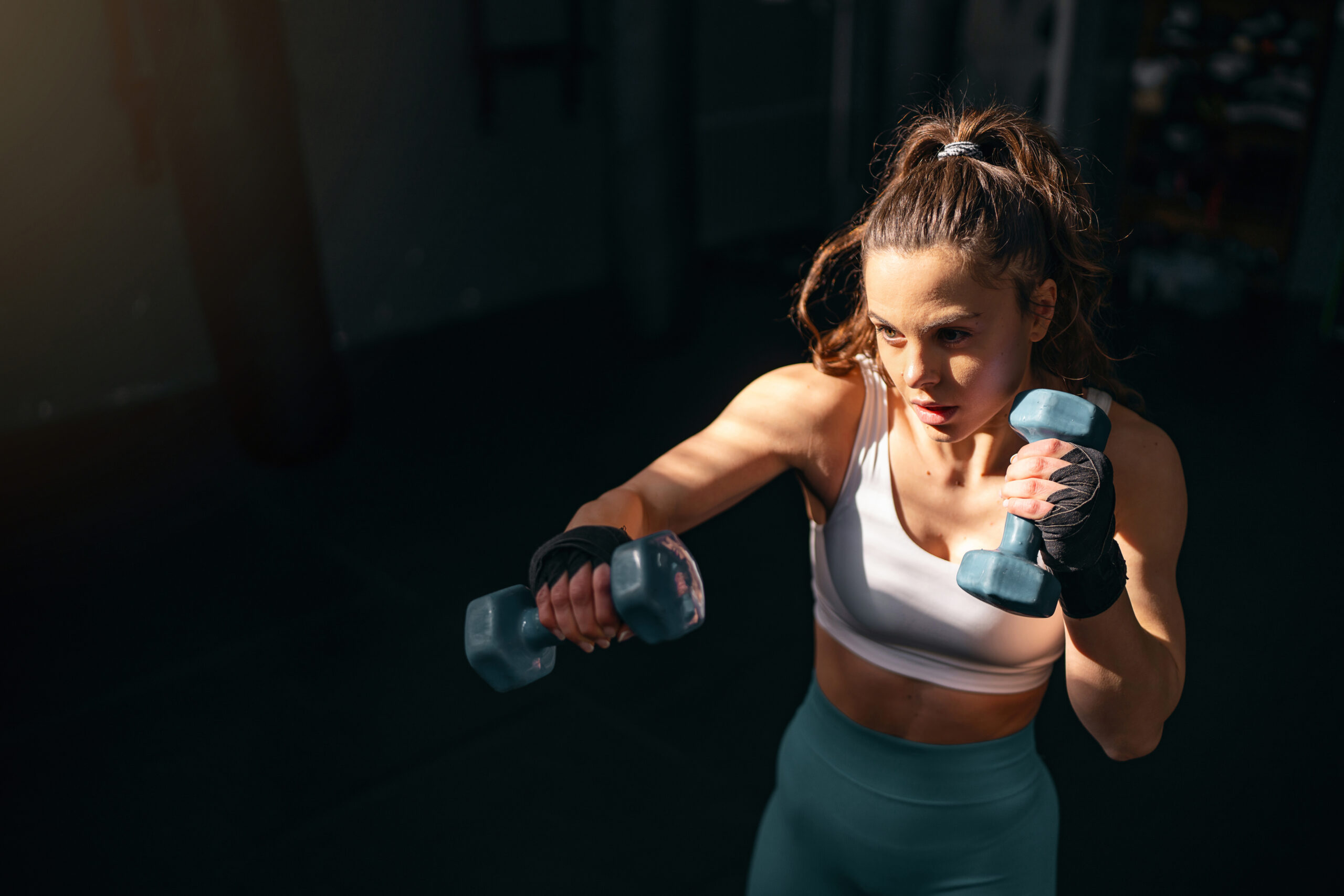 Female kickboxer shadowboxing with dumbbells.