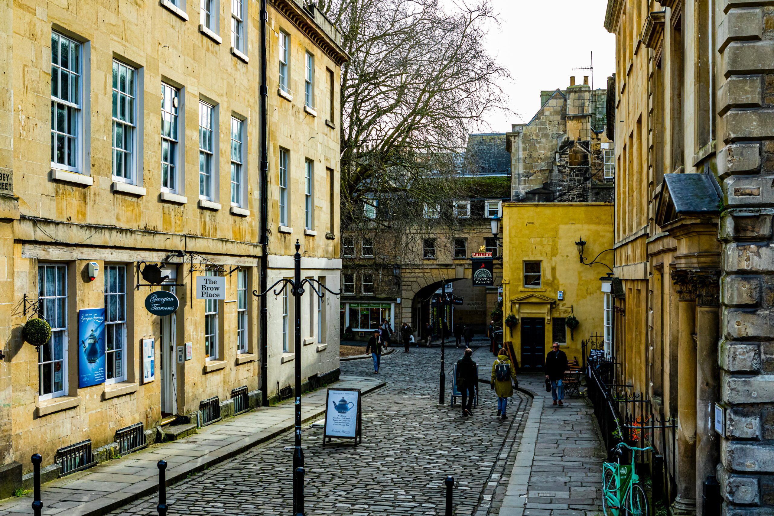 Cobbled street in Bath with a yellow building with georgian facade and shops and a tea house
