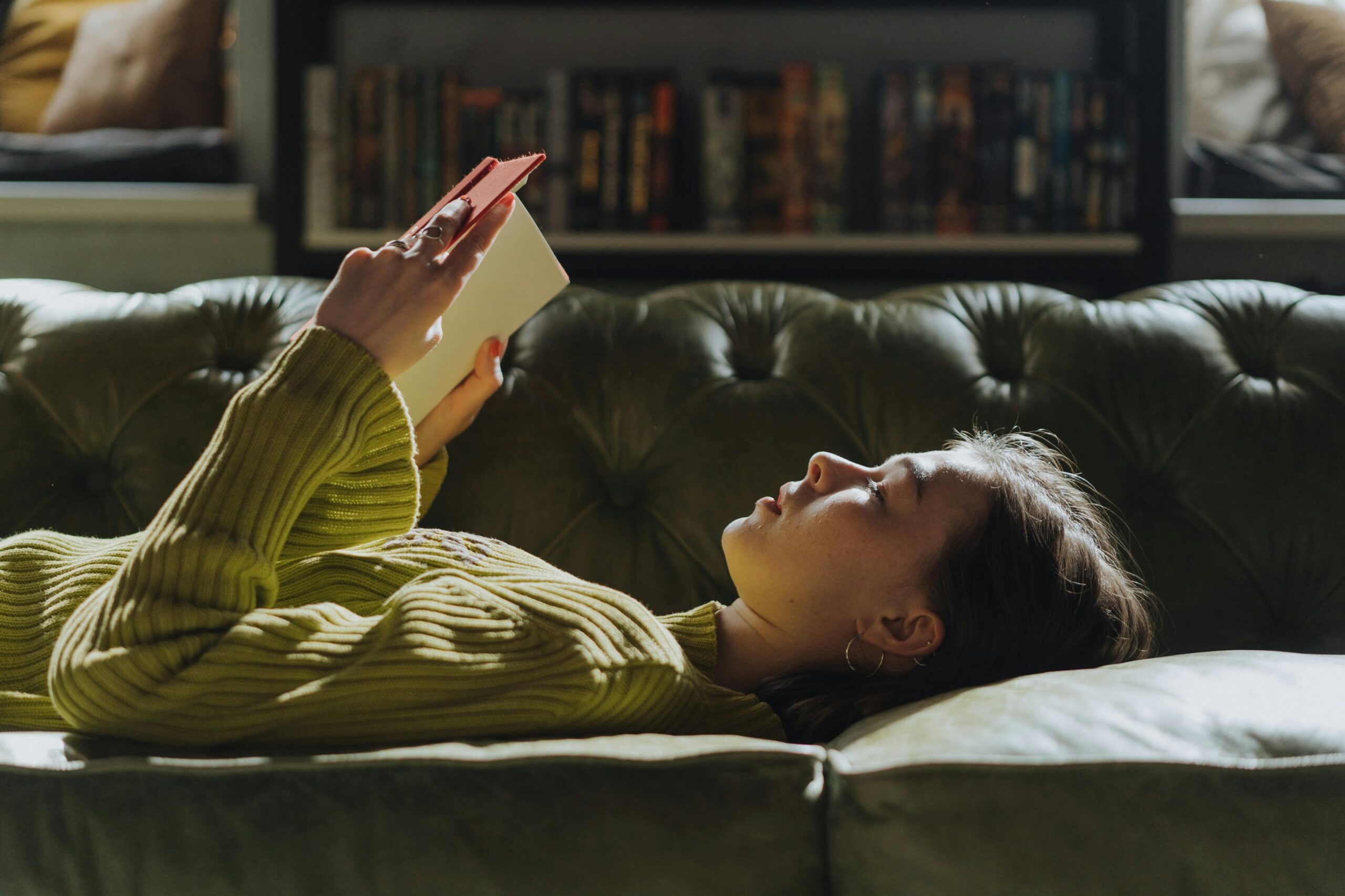 girl lying on sofa in green jumper reading a book