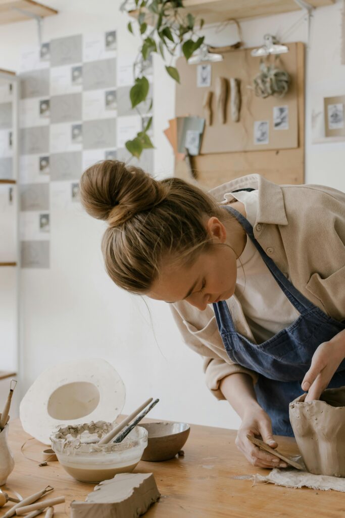 woman standing over table moulding and smoothing clay pot