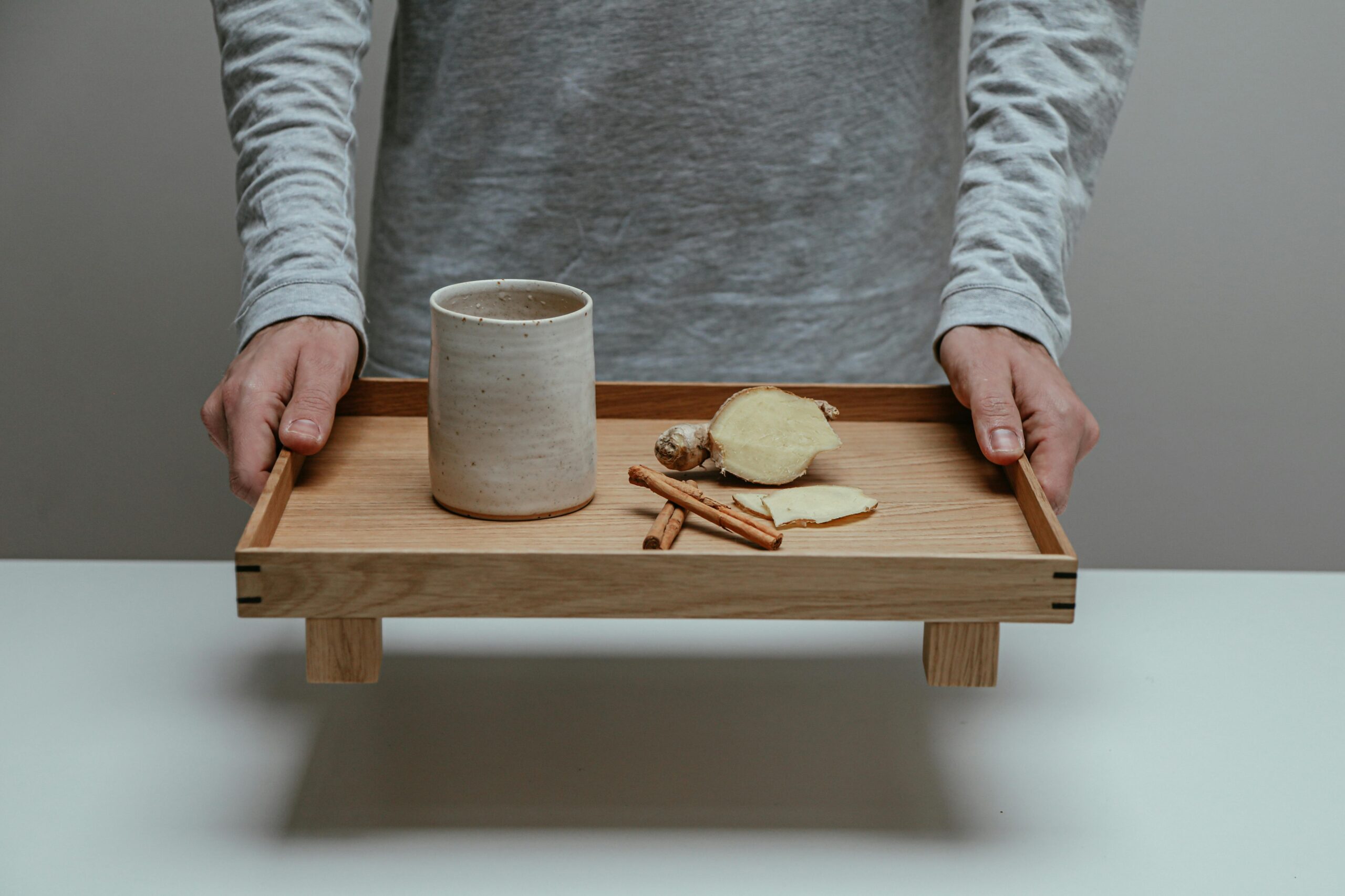 close up man holding wooden tray with cup, tongs and a root veg