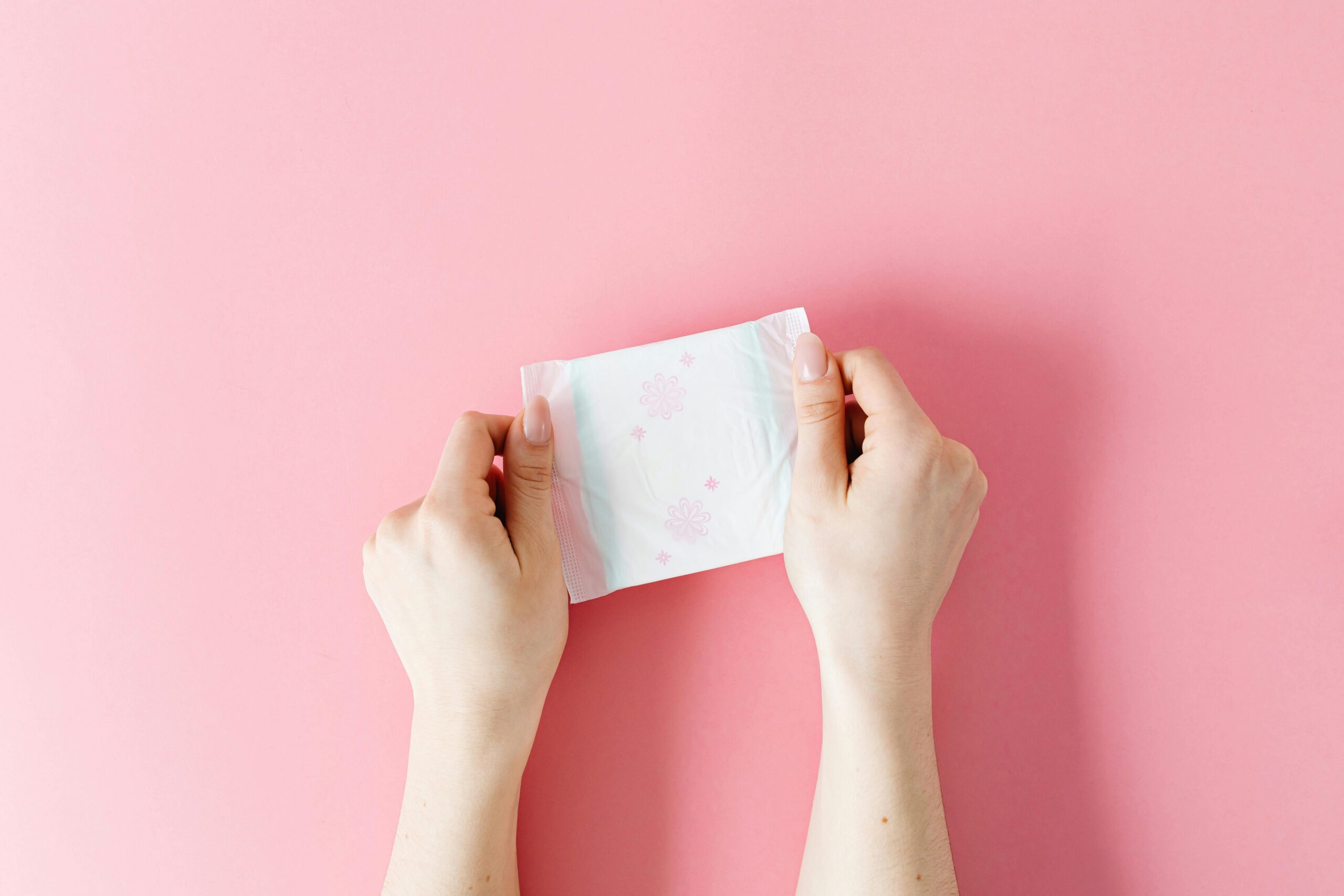 period pad in woman's hands on pink background