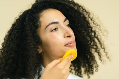 Woman with curly hair using a yellow face sponge.