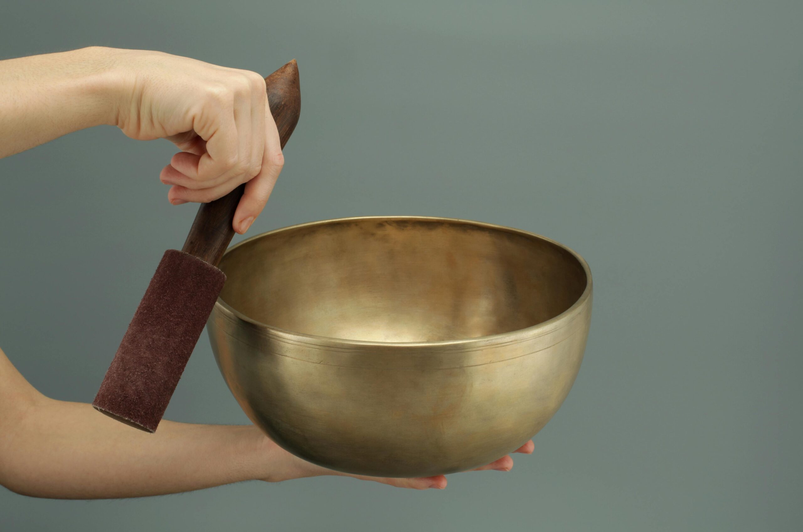 woman's hands holding sound therapy bowl and gong in front of green background