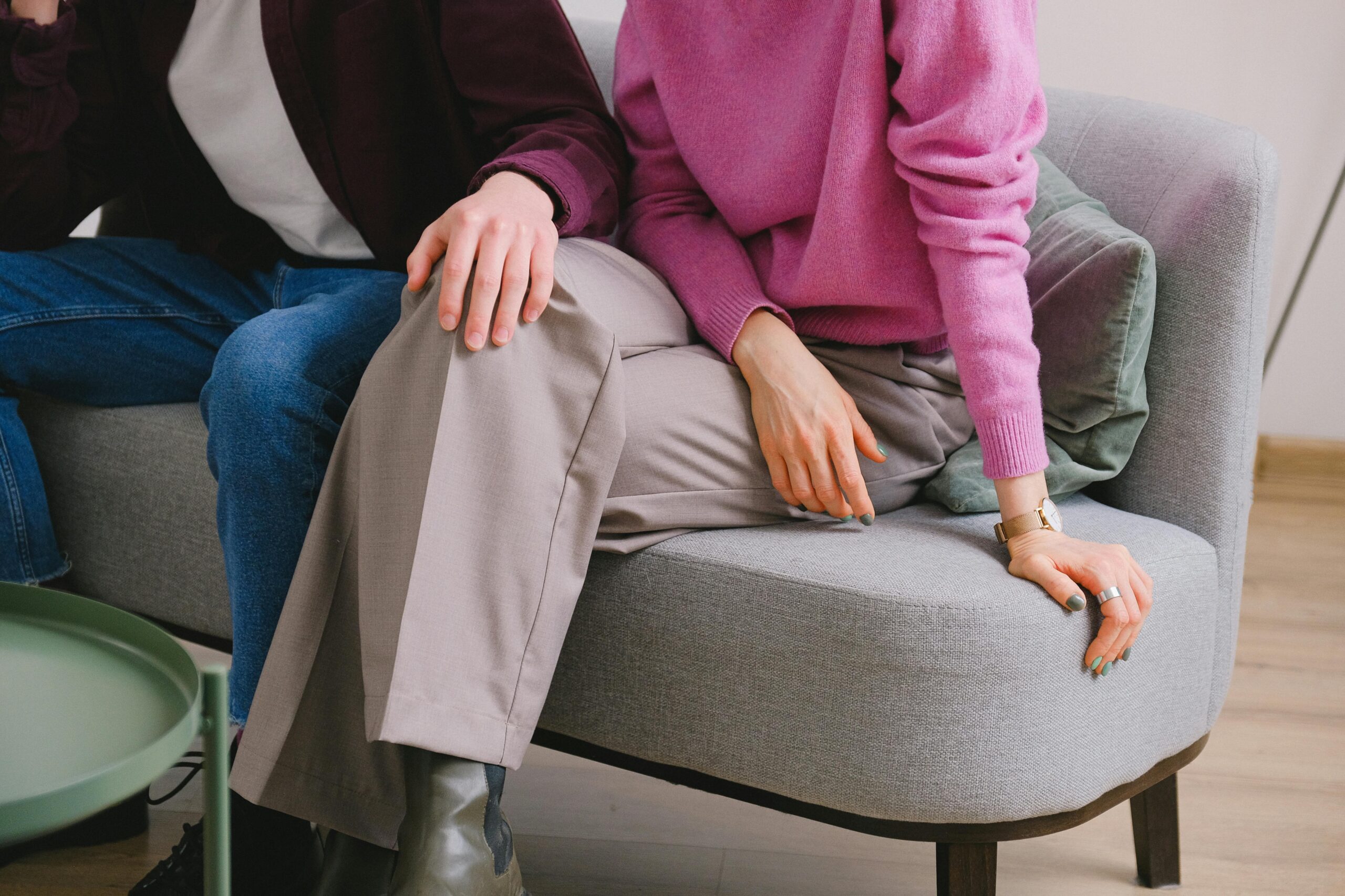couple sitting next to each other on grey sofa with hand on lap and hands on side of sofa
