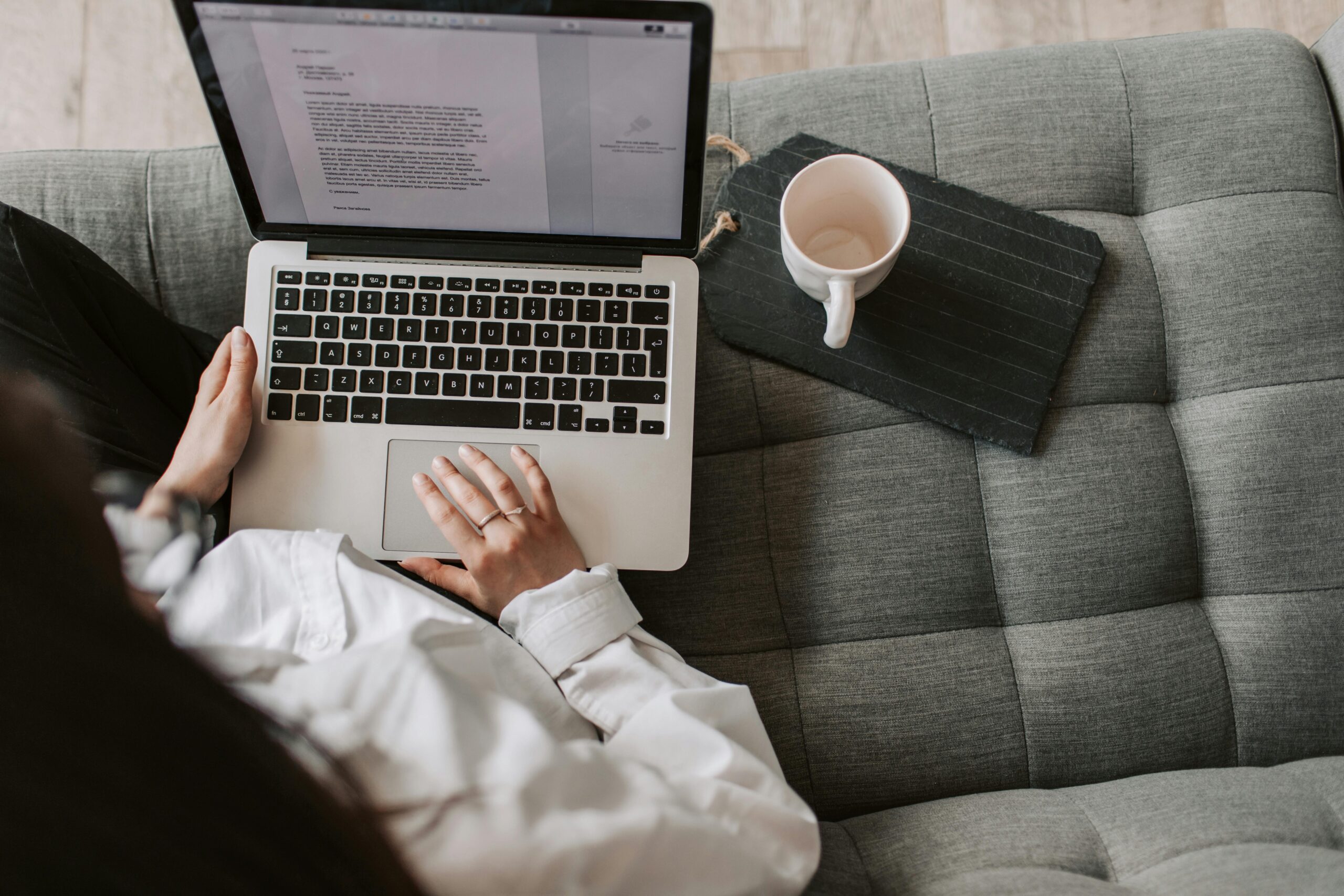 woman sitting on sofa typing on laptop with a mug beside her 