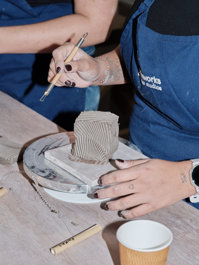 Woman's hands holding paint brush etching into clay