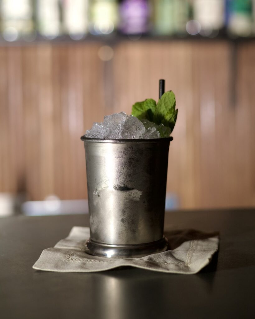 table with cocktail on top in silver cup with mint leaf and straw