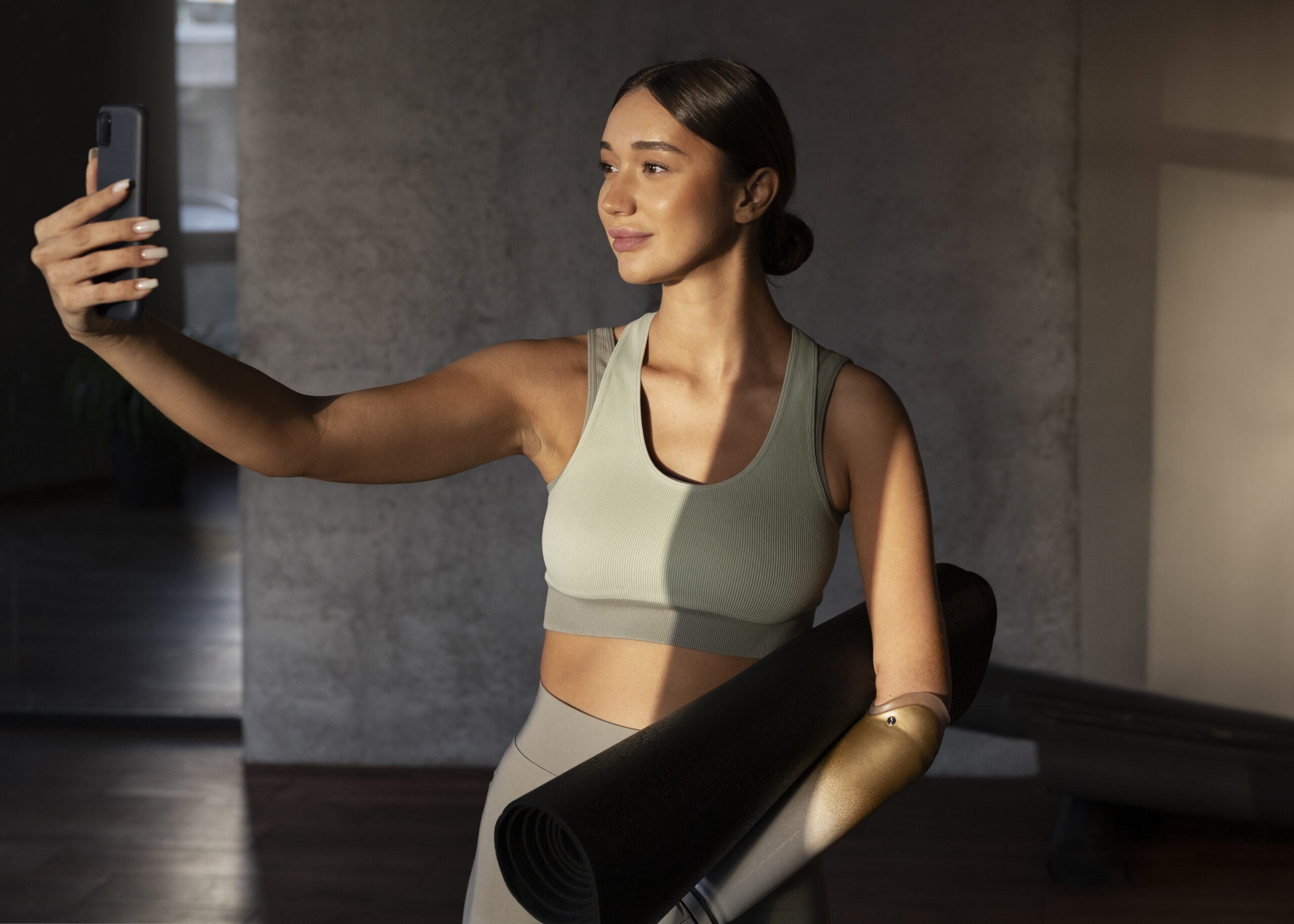 woman in fitness studio taking a selfie with a Pilates mat under her arm