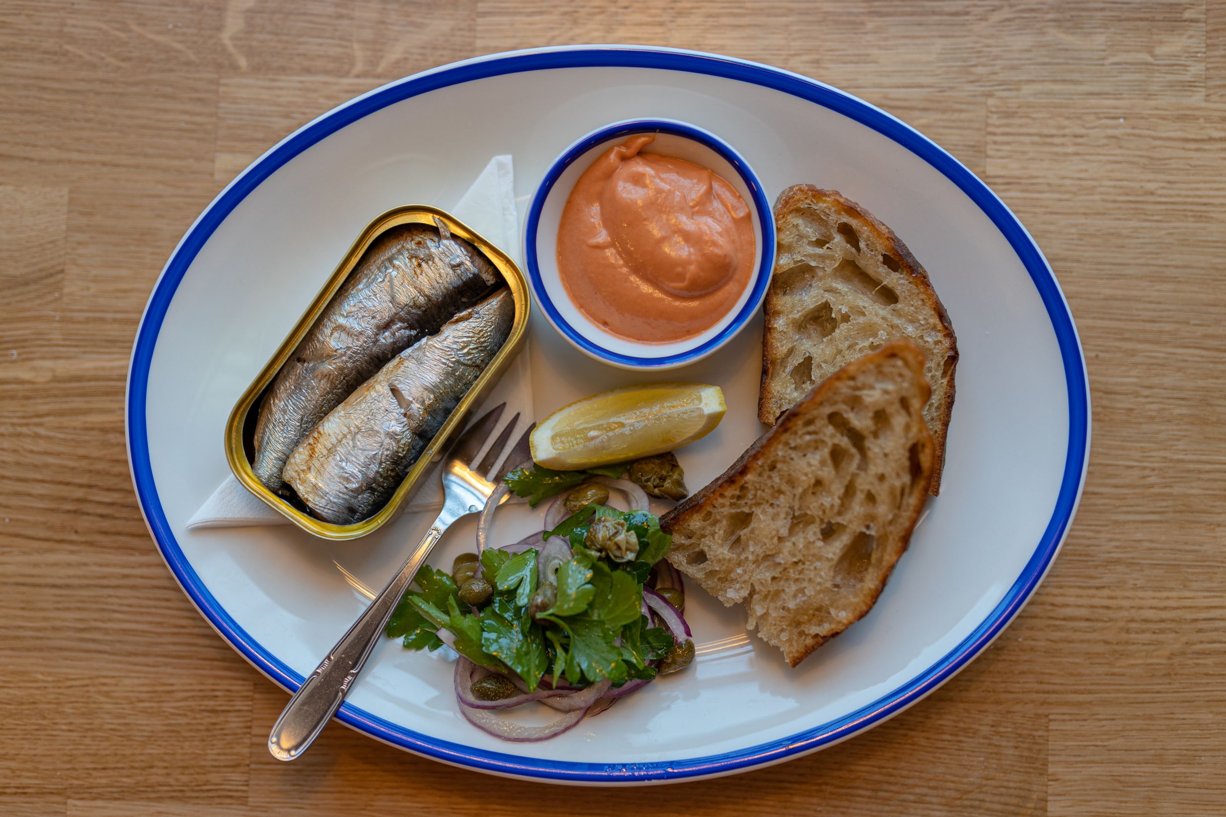 Plate with tinned sardines, toast and orange mayo sauce