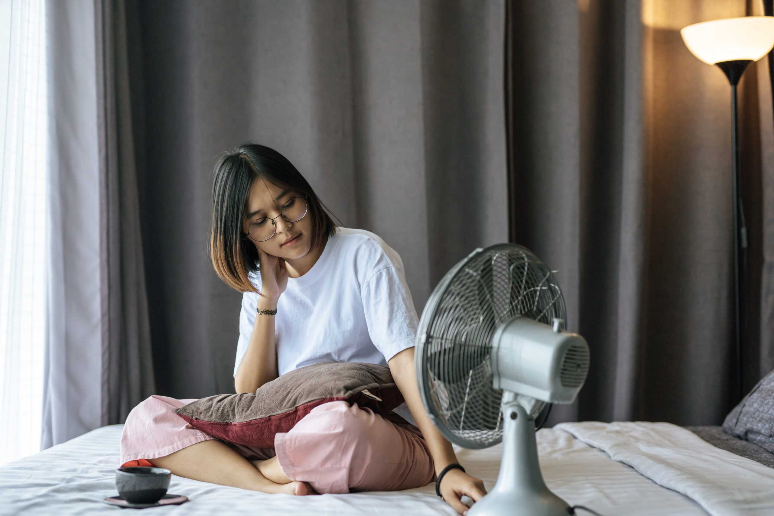 girl sitting and drinking coffee in the bedroom and a pillow on her legs.