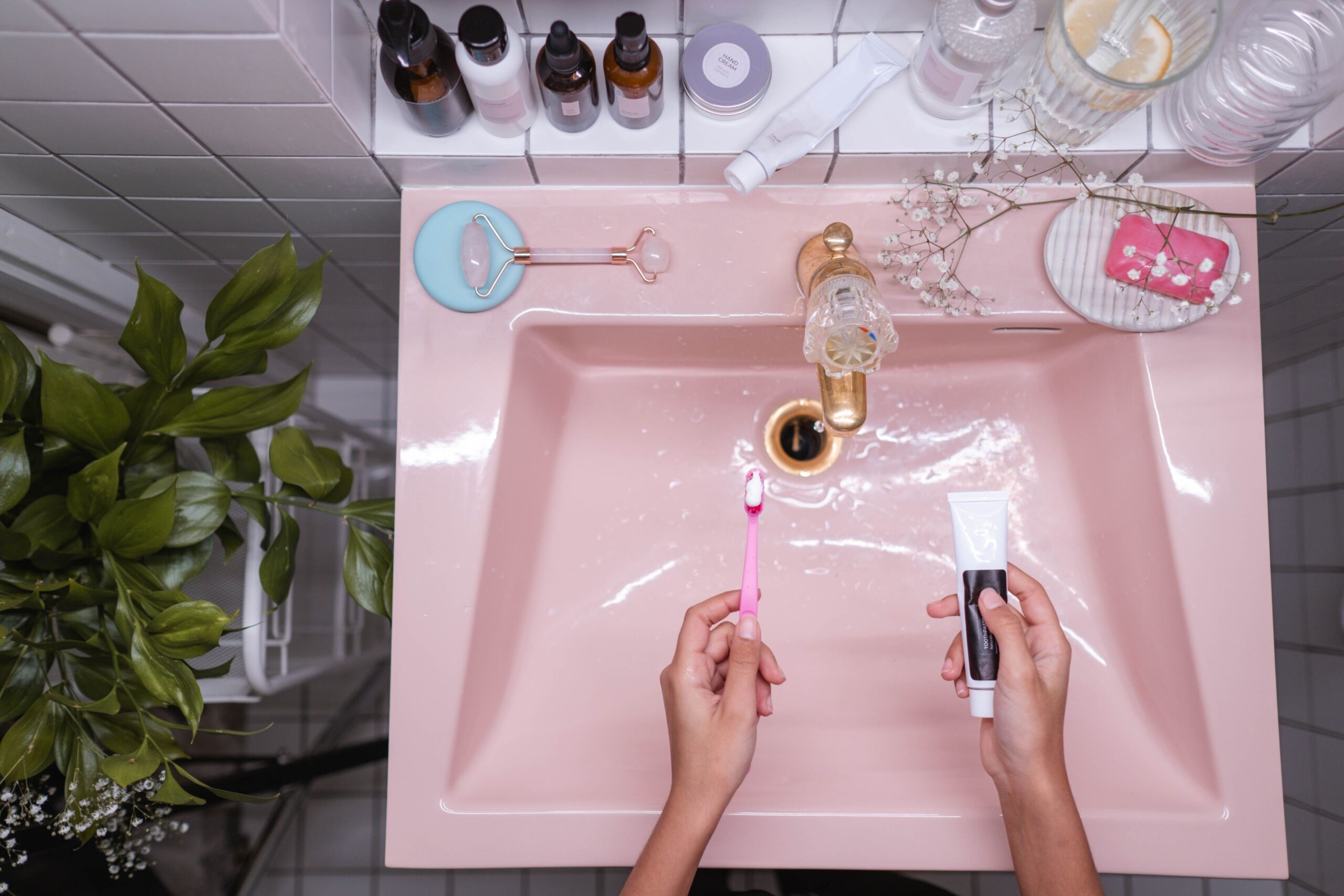 women's hand holding a toothbrush and toothpaste over a slightly pink sink