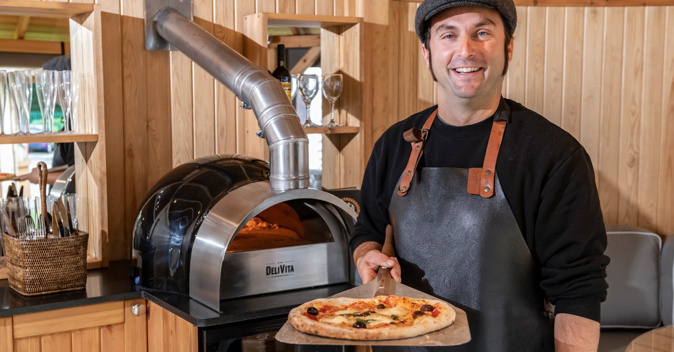 A Delivita chef presents a pizza he's just made in a Crown Pavilions garden room.