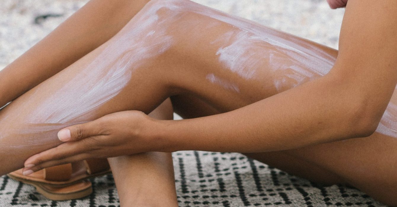 A woman applies sun cream to her body.