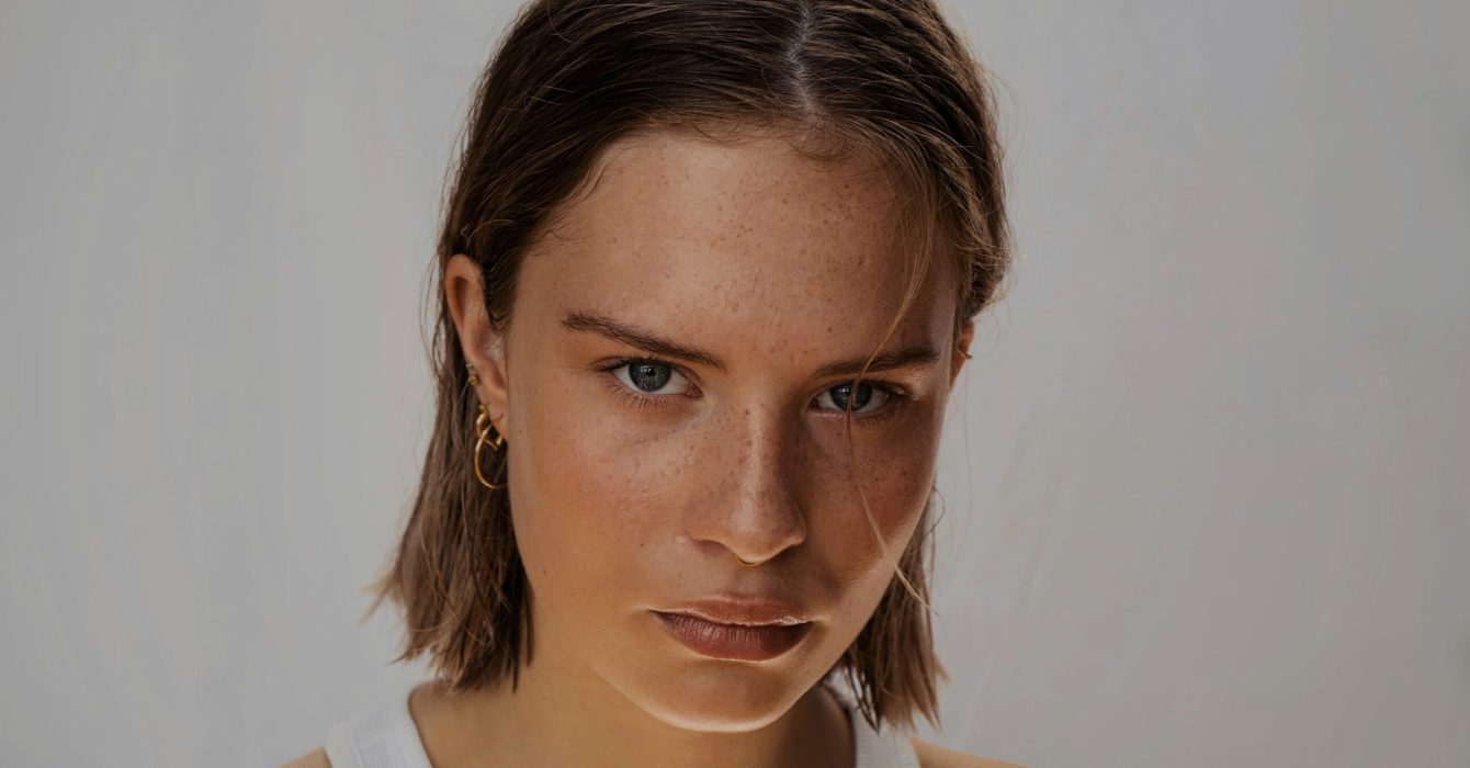 A woman with a heavy brow looks into the camera lens