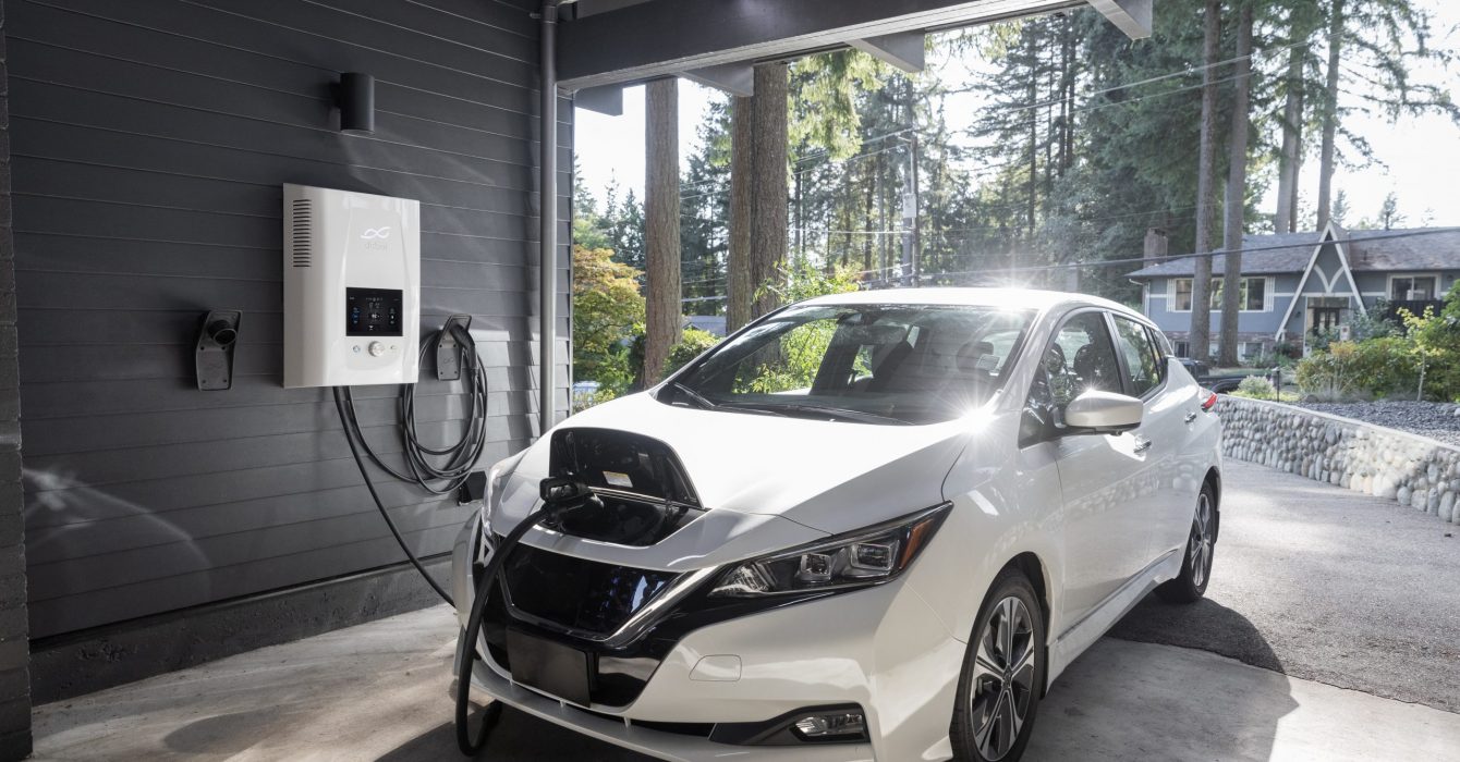 Inside a home garage, a white car is being powered up by an EV charger.
