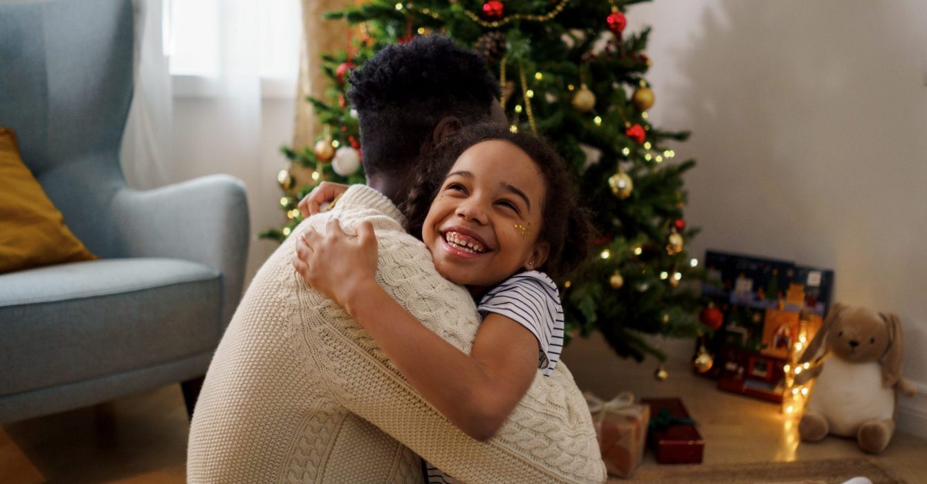 A young child hugs her father elated after receiving her Christmas gift