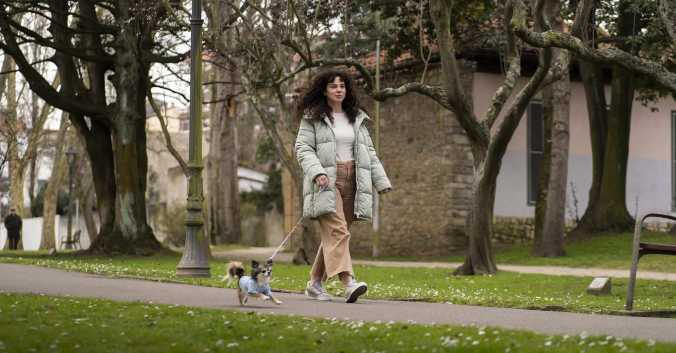 Woman in long coat walking in a park with her dog