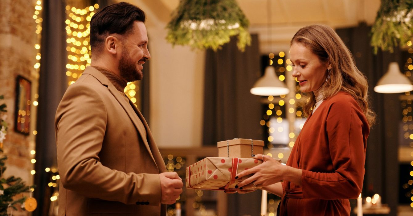 A woman in red gives two wrapped Christmas presents to her friend