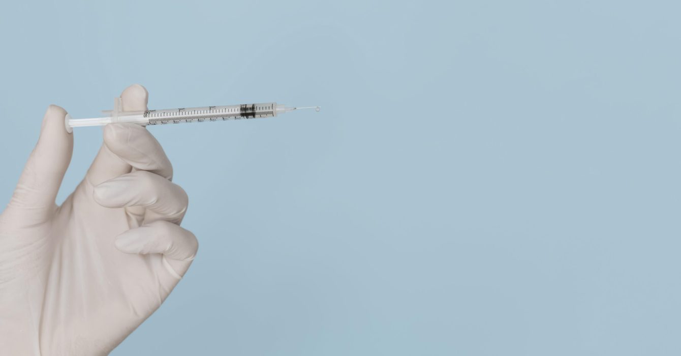 a needle ready to inject polynucleotides held against a blue background