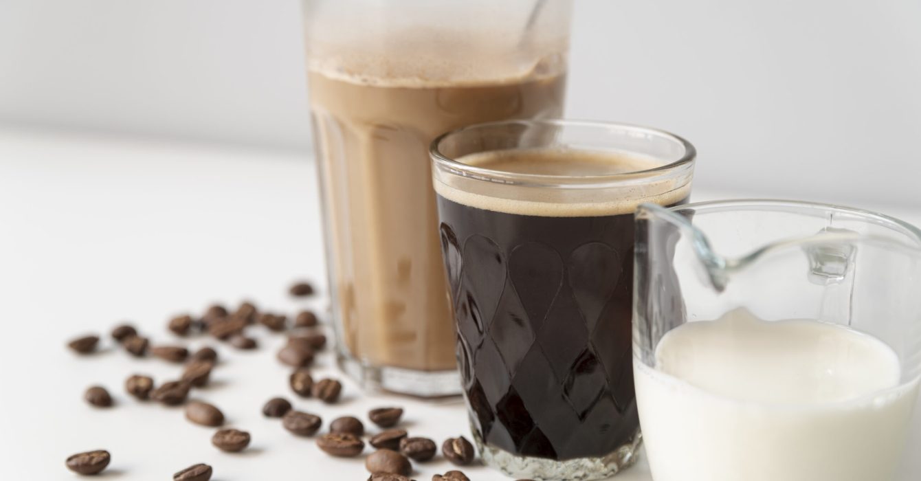 an iced coffee, a black coffee and milk all sit by by side in glasses on a white table