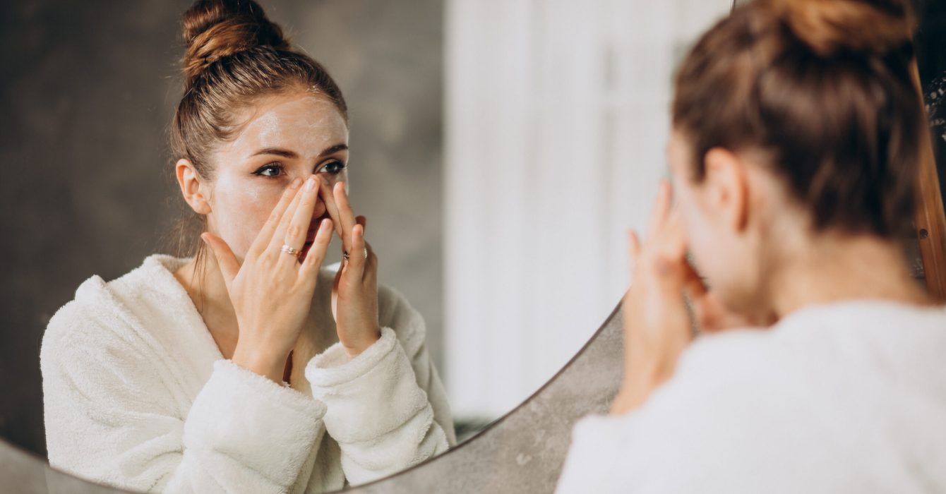 A woman looks in the mirror as she washes her face with a milky cleanser