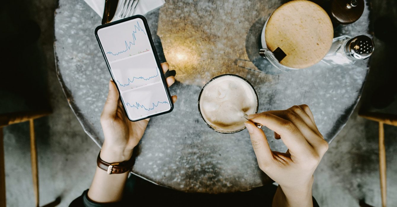 Overhead view of a woman checking her investments on a smartphone during a coffee break