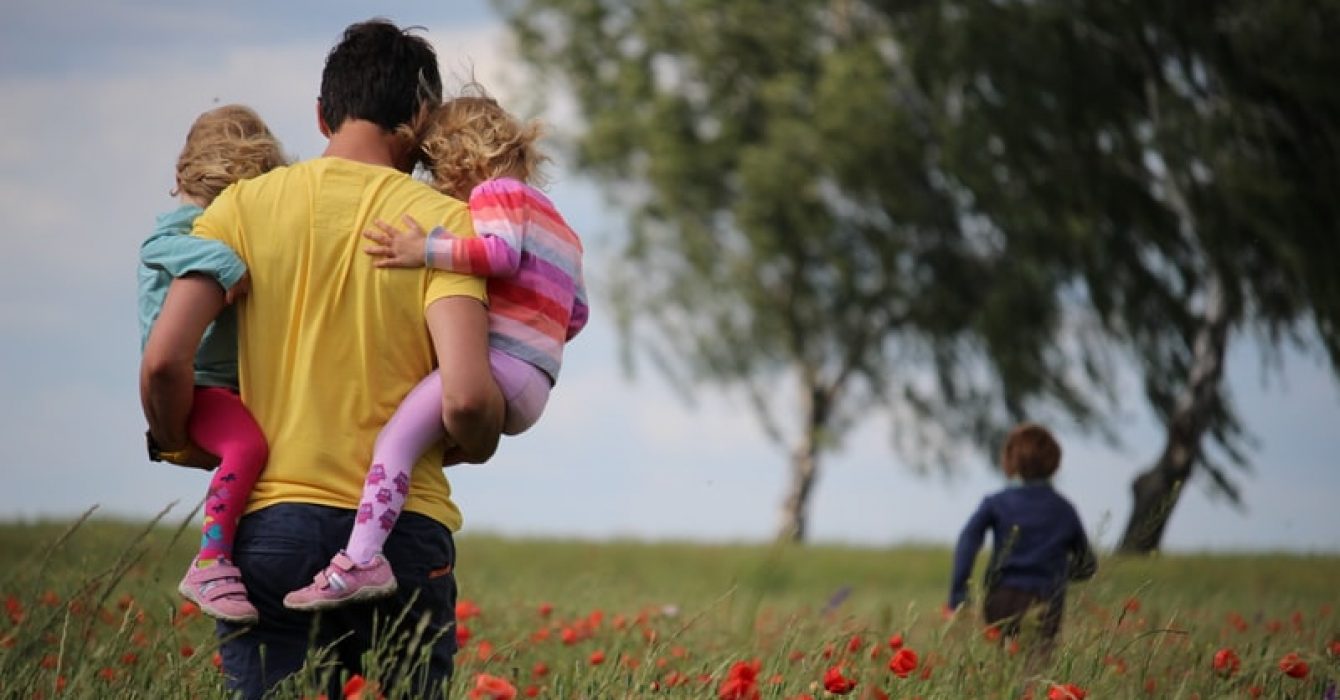 A father walks with his children through a field.