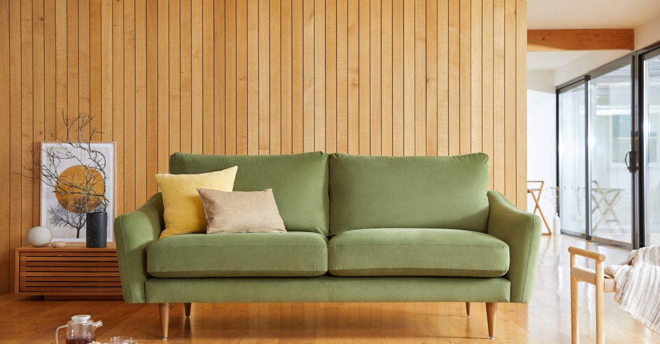 Living room with olive green sofa, yellow and beige pillows, wooden wall and floor