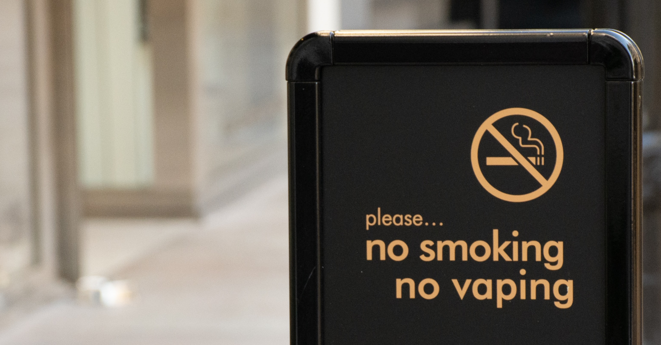 A black street sign with an anti-smoking/vaping sign and yellow letters which read, 'no smoking, no vaping'.