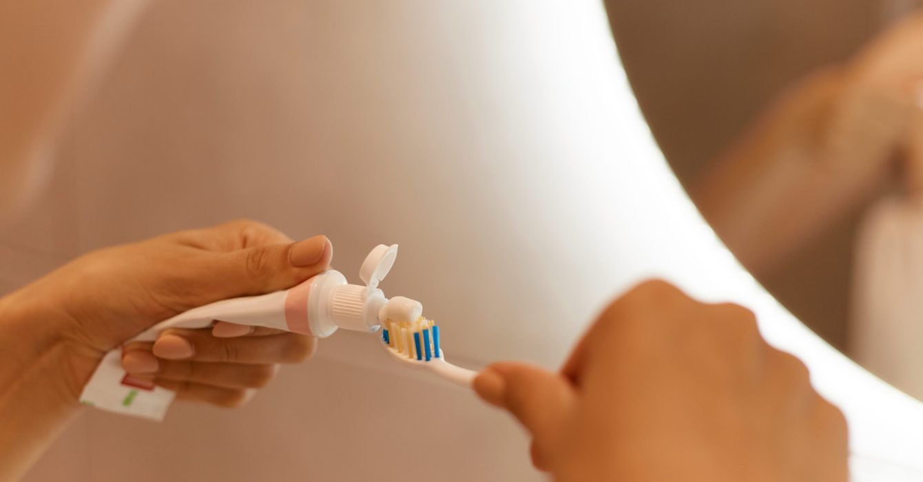 Close up portrait of woman hands in front of mirror in bathroom, holding toothpaste and toothbrush, squeezes the toothpaste out of the tube.