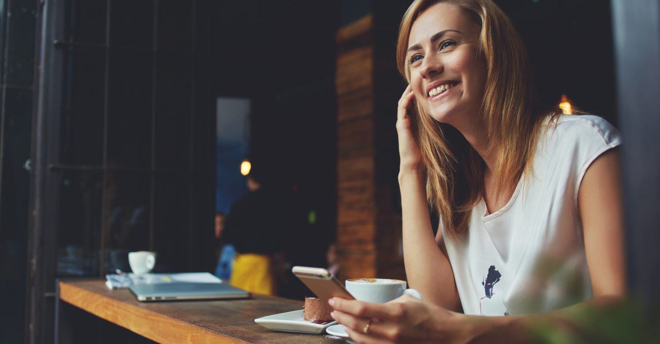 On a coffee break, a young blonde woman checks her saving app on her iPhone.