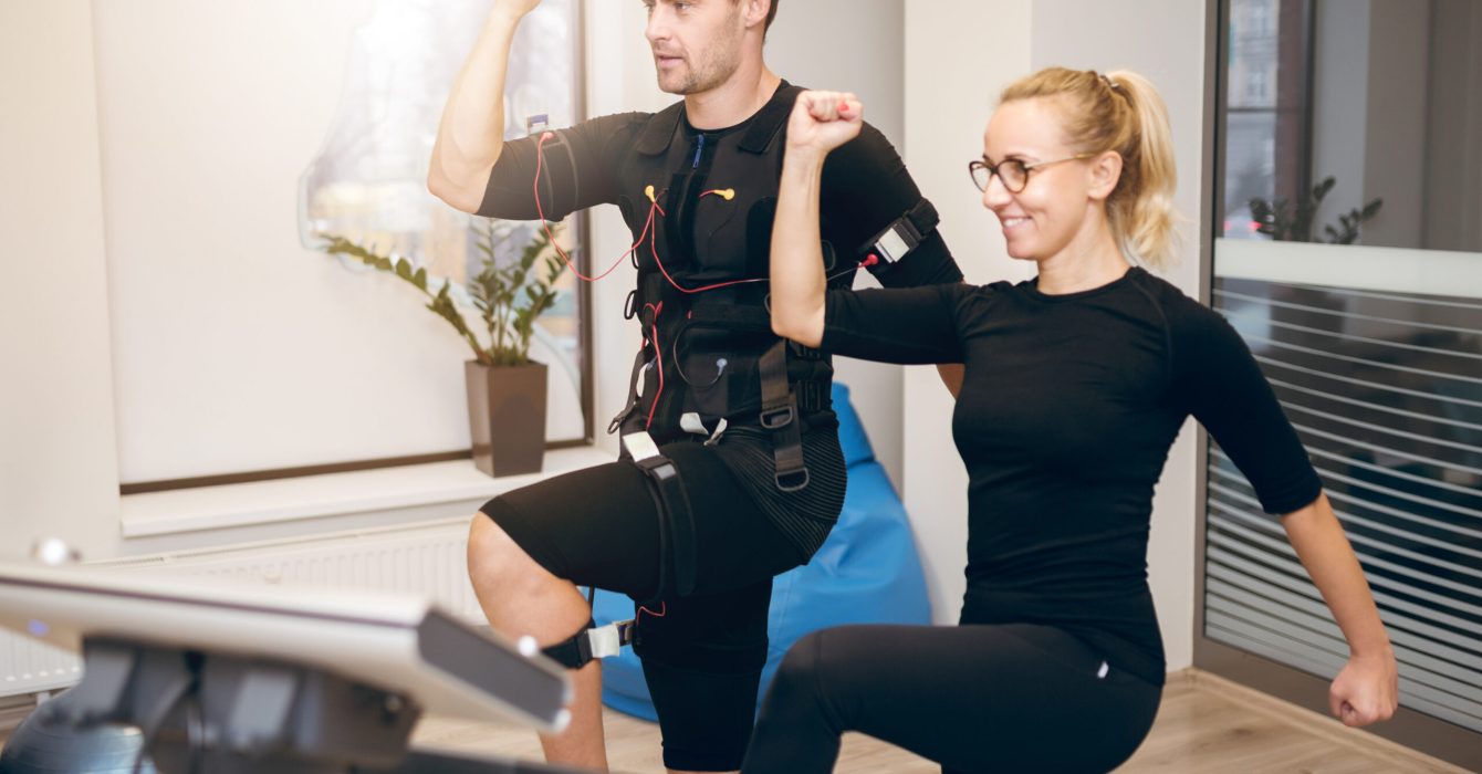 A female trainer provides guidance to an athlete in the middle of his EMS training.