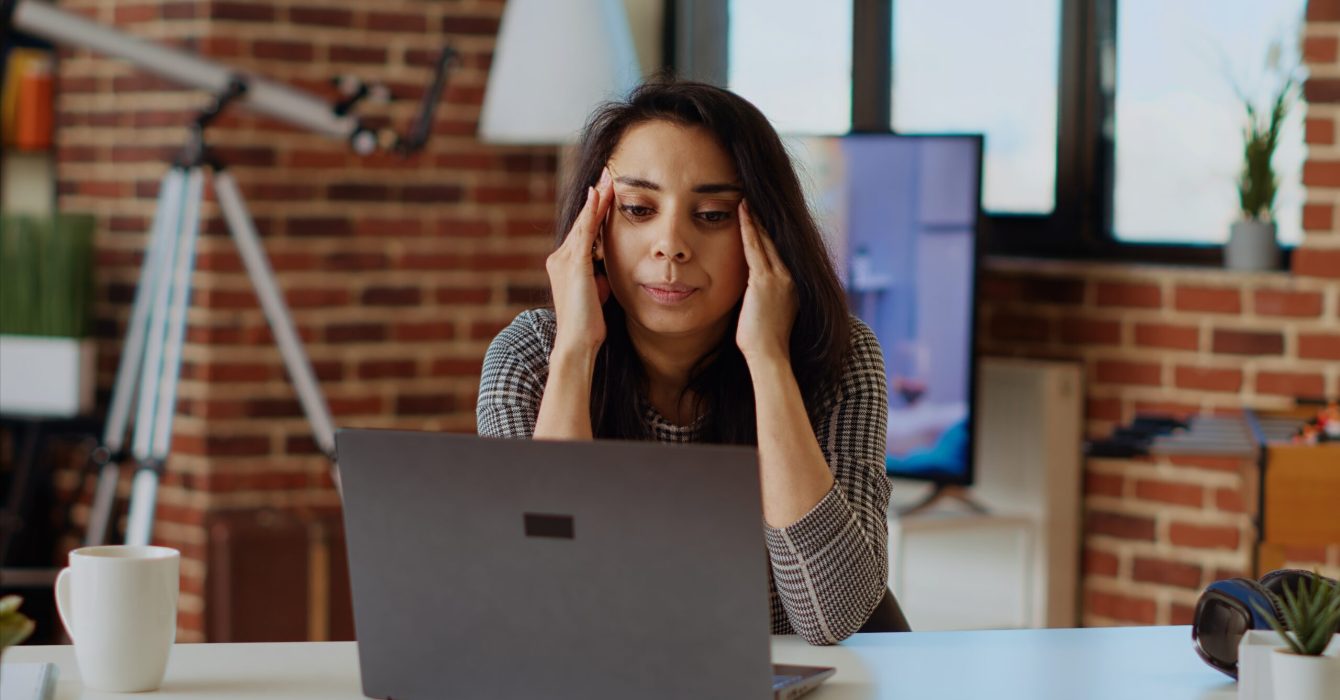 Self employed woman feeling ill, struggling to concentrate while working from home, hurting from headache. Exhausted freelancer suffering from sickness and stress while working on laptop, camera B