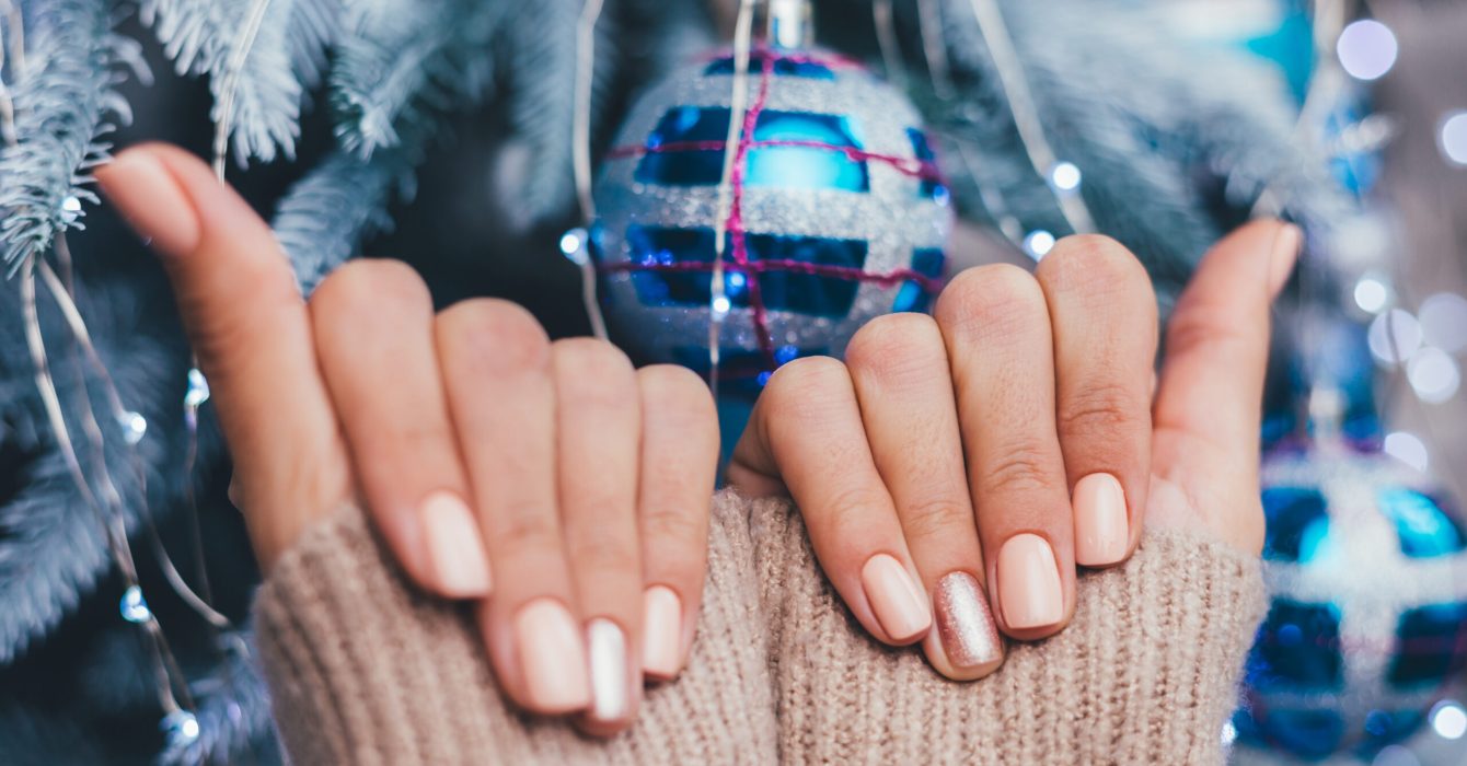 Female hands with Christmas new year nail design. Nude beige nail polish manicure, one finger shiny golden bronze