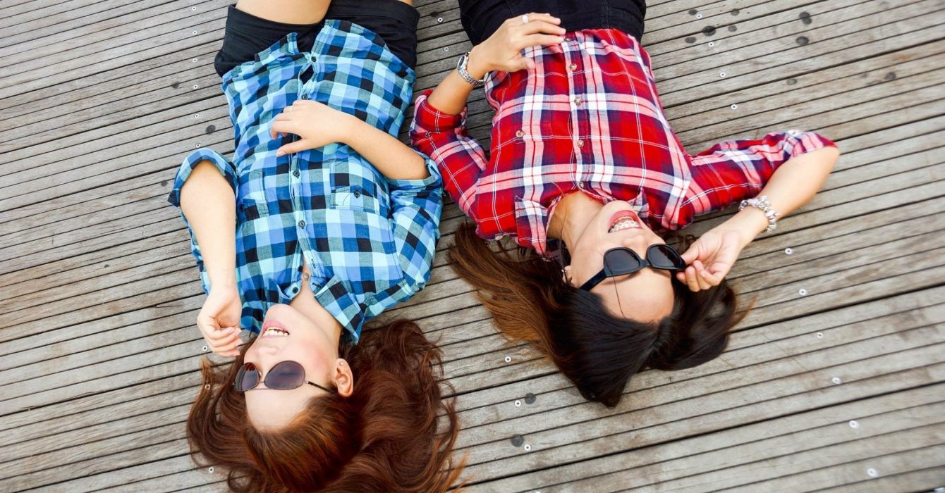 Lying on the ground, two friends hang out with their shades on.