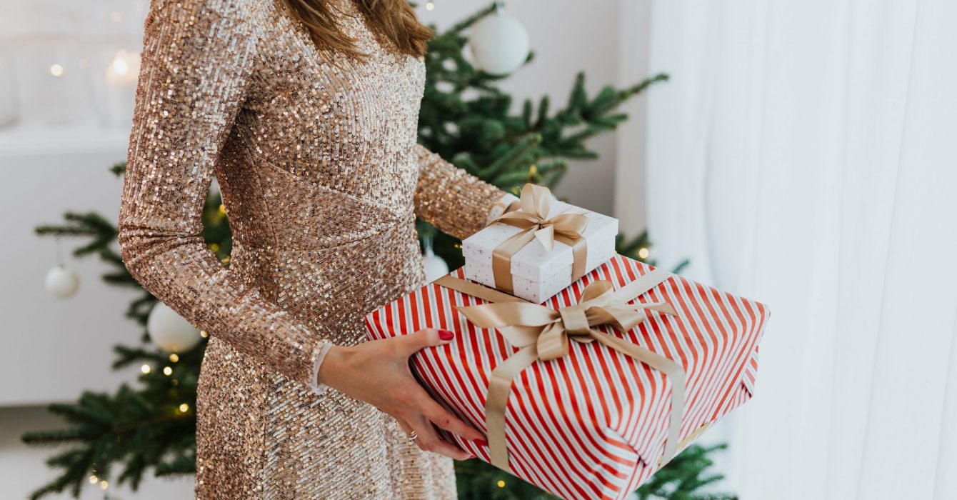 A woman in a gold dress holds a wrapped Christmas present