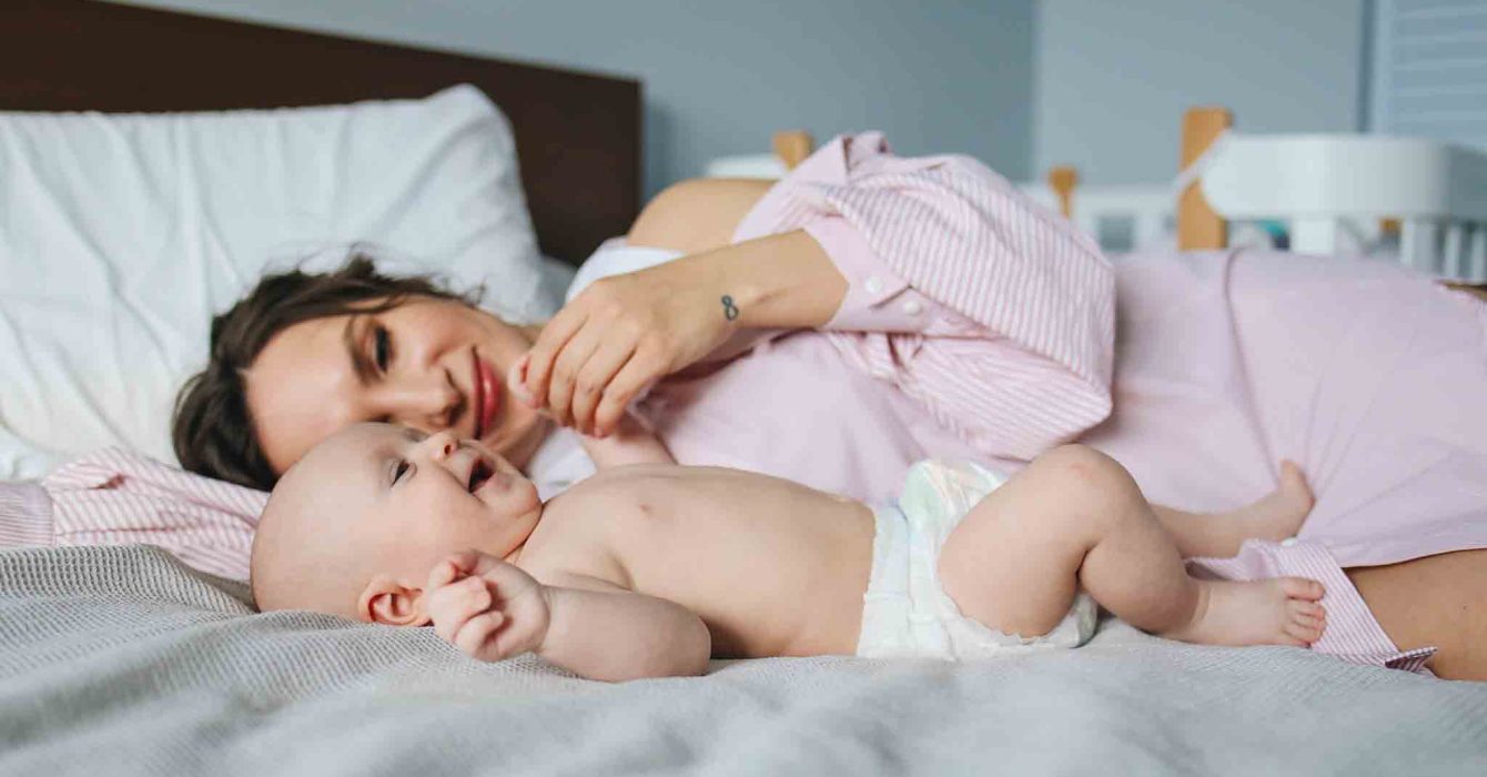 Mum cuddling with smiley newborn on bed