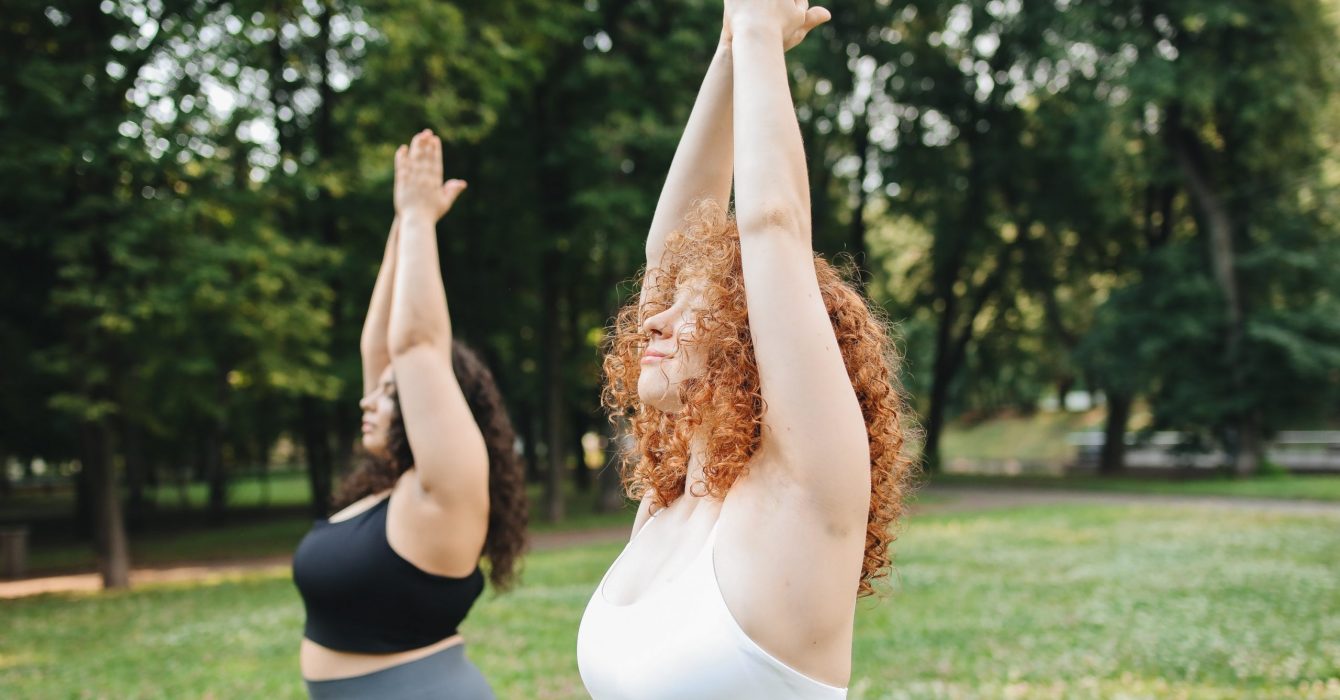 Two overweight women practise yoga in the park.