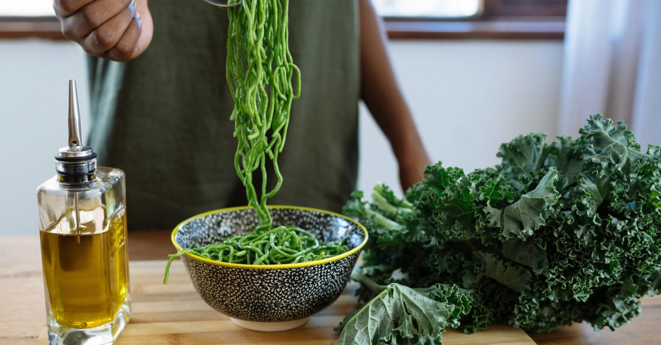 A fork full of green spaghetti is held up to the camera