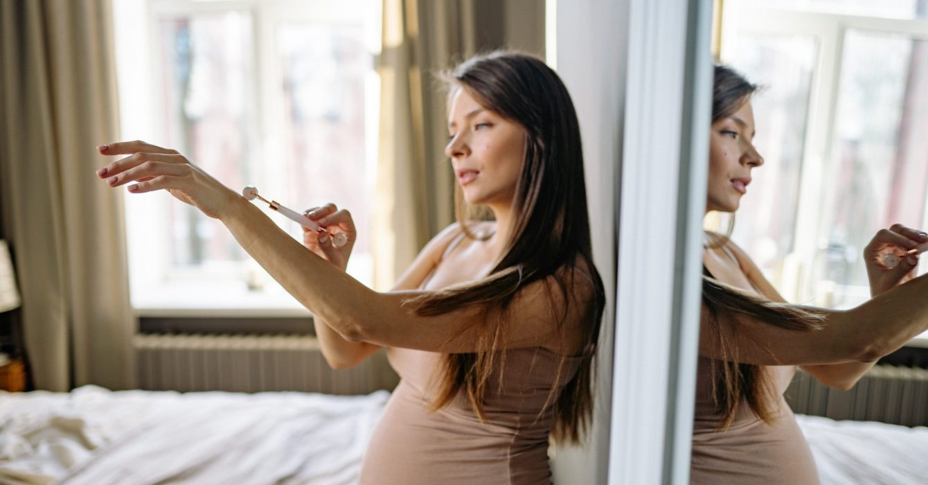 A young pregnant woman moistures her arms.