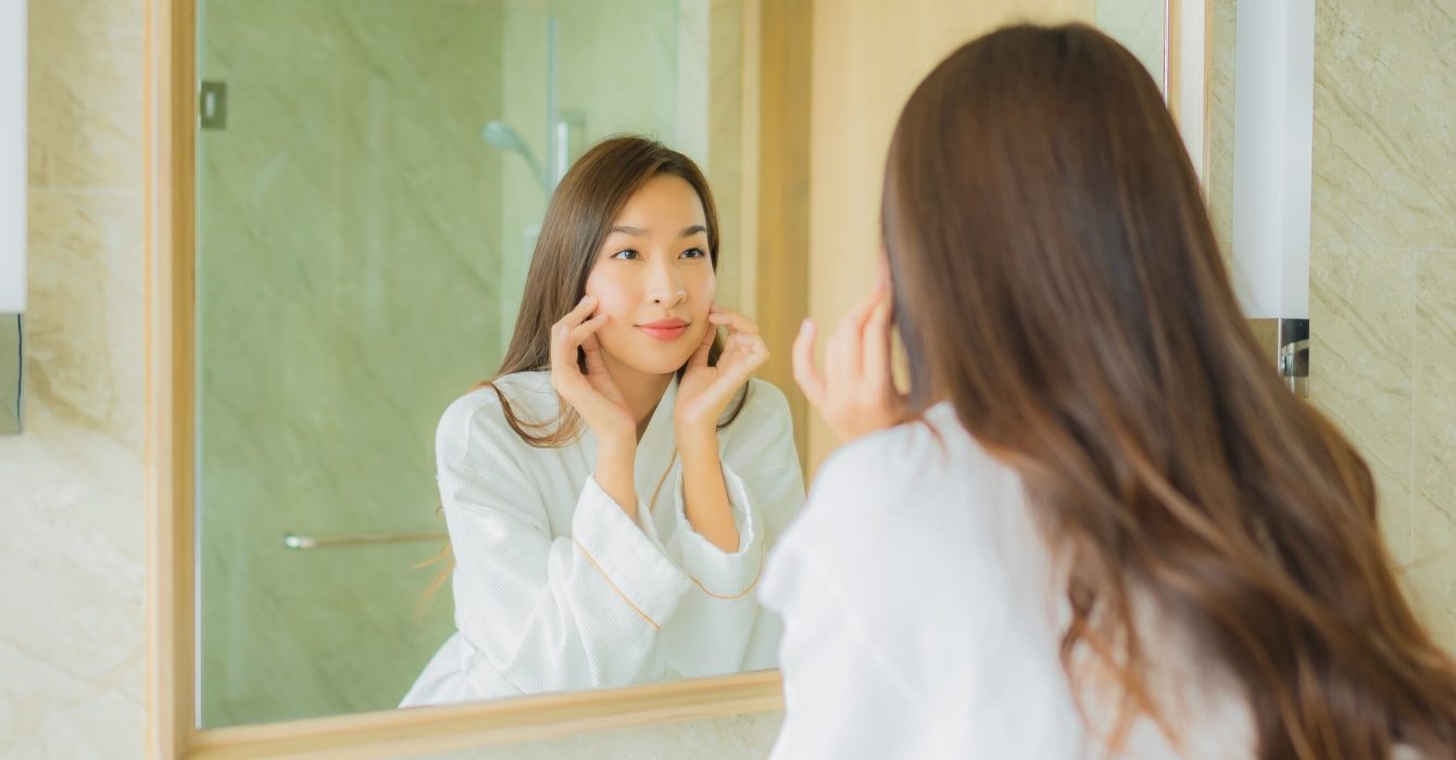 Portrait beautiful young asian woman check up face in bathroom interior