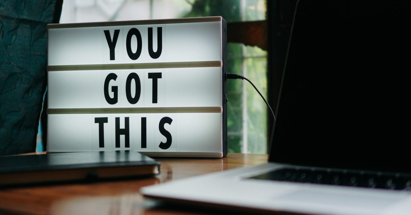 A small electric sign on a desk with a MacBook reads: 'YOU GOT THIS'.