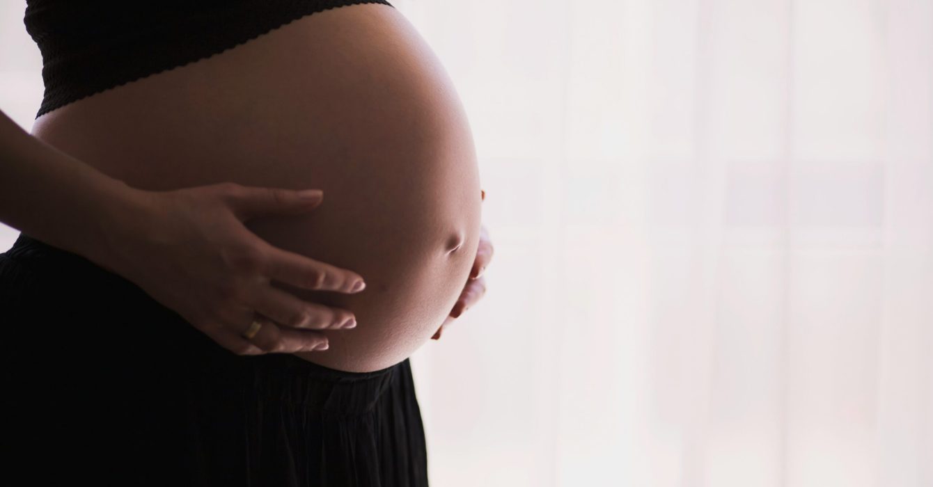 dark close up of a woman from the side holding her bare pregnant stomach